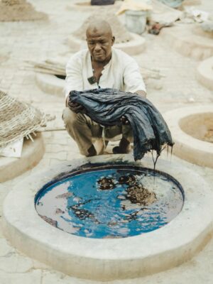 A craftsman skillfully dyeing fabric in a traditional outdoor dye pit.