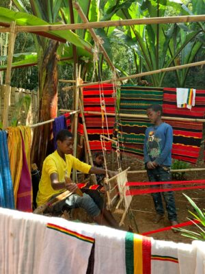 Young men weaving colorful textiles outdoors, showcasing traditional craft.